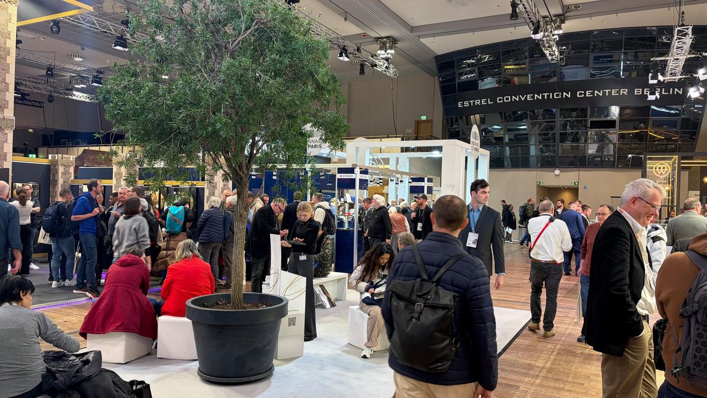 Blick durch die Messehalle mit vielen Besuchern, Sitzbereichen und begrünten Elementen auf der World Money Fair